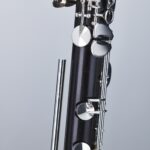 Detailaufnahme einer Hammerschmidt OH-810 Klarinette, bestehend aus schwarzem Holz mit silberfarbenen Klappen, Schrauben und einem separaten, metallischen Stab, vor einem einfarbigen, hellen Hintergrund.