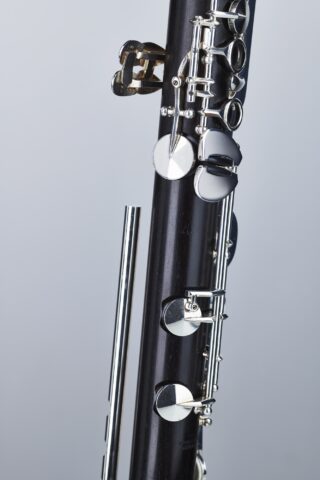 Detailaufnahme einer Hammerschmidt OH-810 Klarinette, bestehend aus schwarzem Holz mit silberfarbenen Klappen, Schrauben und einem separaten, metallischen Stab, vor einem einfarbigen, hellen Hintergrund.